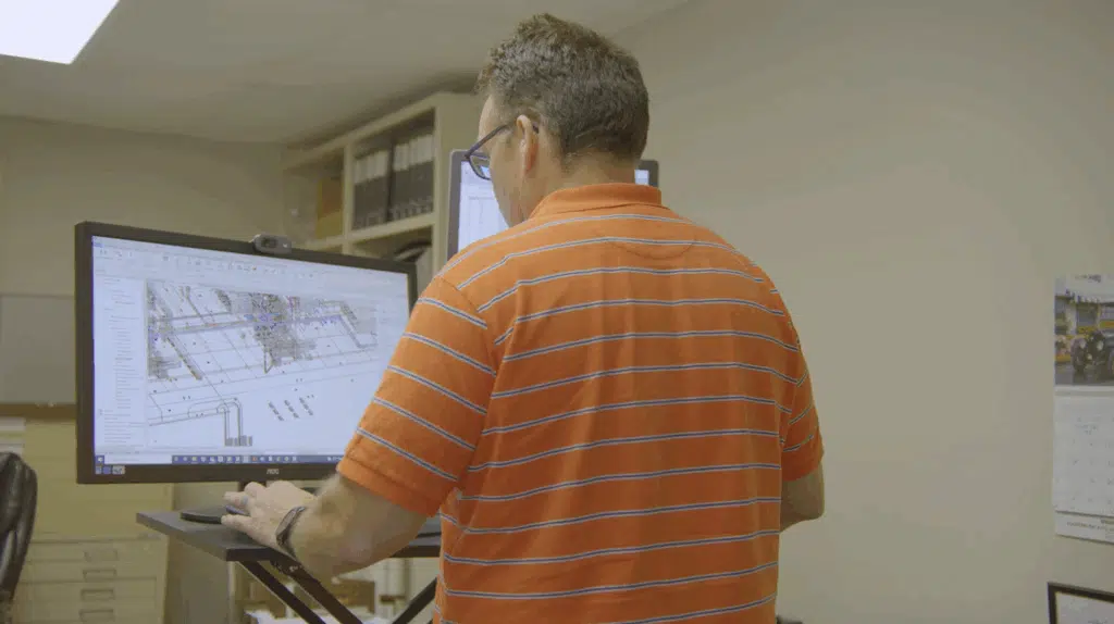 A male engineer at a standing desk looking at schematics on a monitor