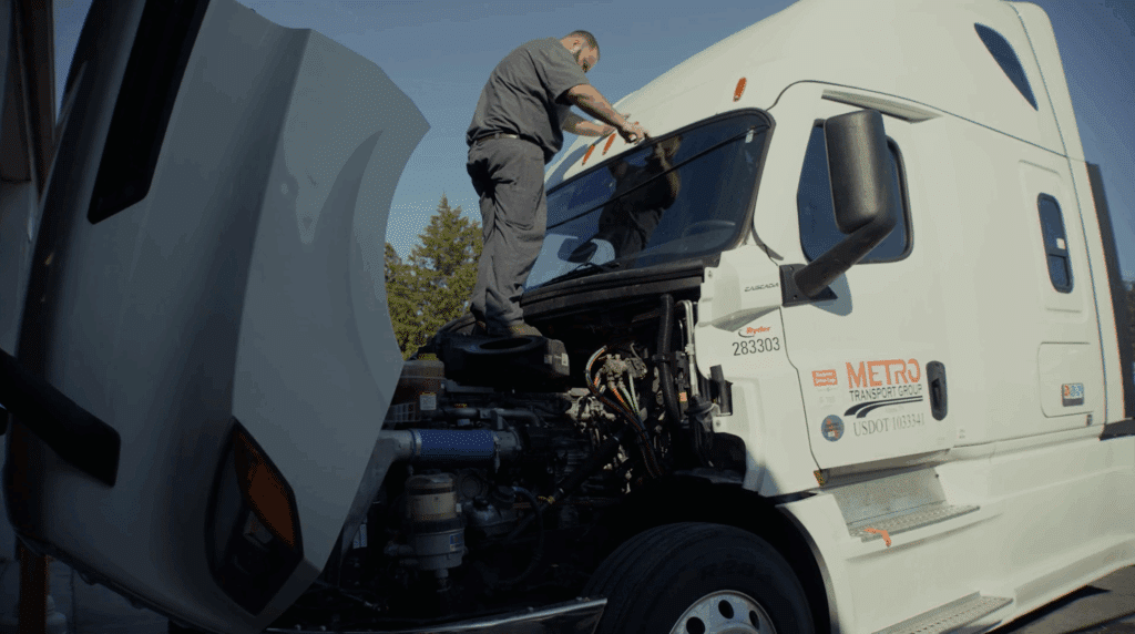 A professional truck driver on top of his rig inspecting the engine with the hood open