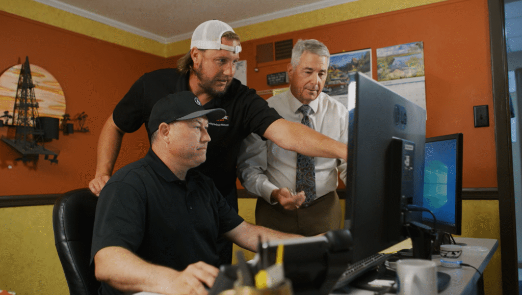 Three men in a warehouse stand by a large teal Marmo Meccanica industrial stone-polishing machine, monitoring its progress.