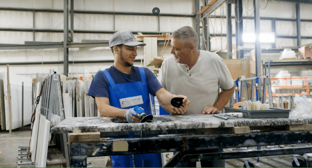 Iowa Countertops. Grimes, IA. A3. 2 men working on marble countertops in a garage facility smiling structured improvement process