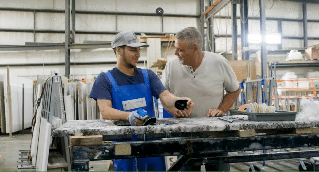 Iowa Countertops. Grimes, IA. A3. 2 men working on marble countertops in a garage facility smiling structured improvement process