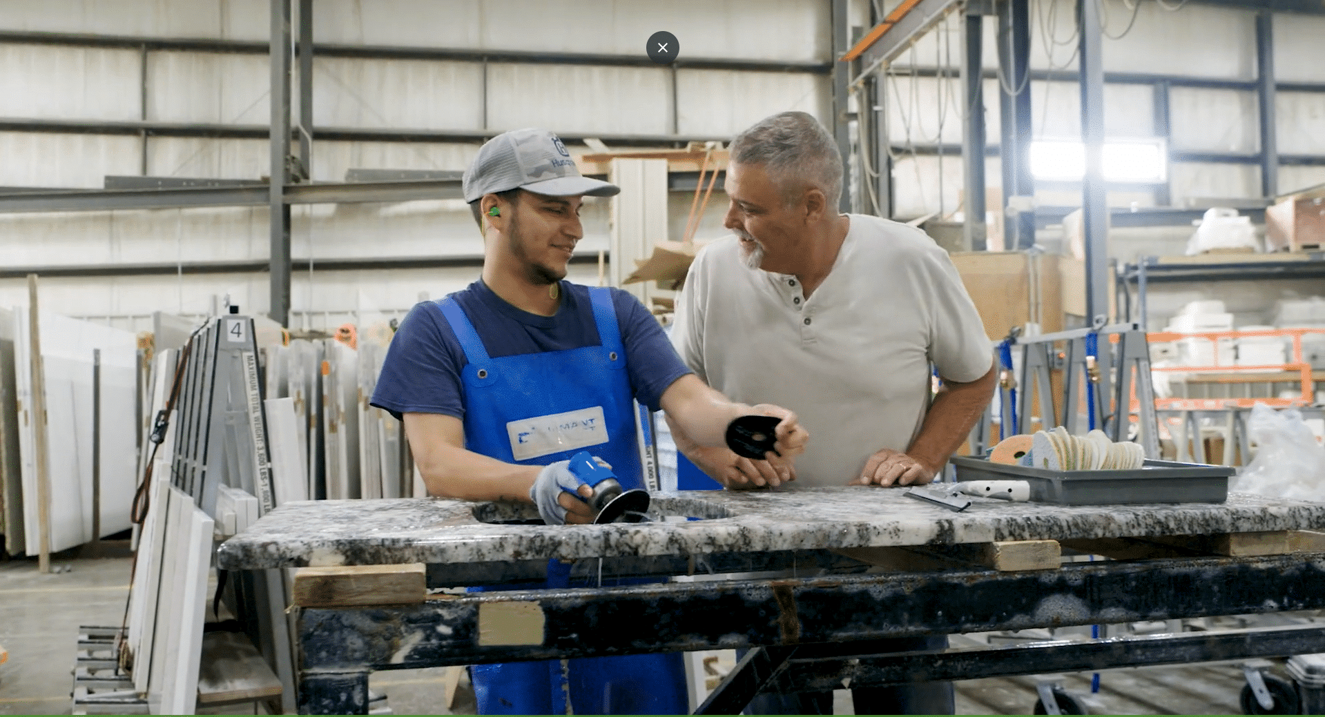 Iowa Countertops. Grimes, IA. A3. 2 men working on marble countertops in a garage facility smiling
