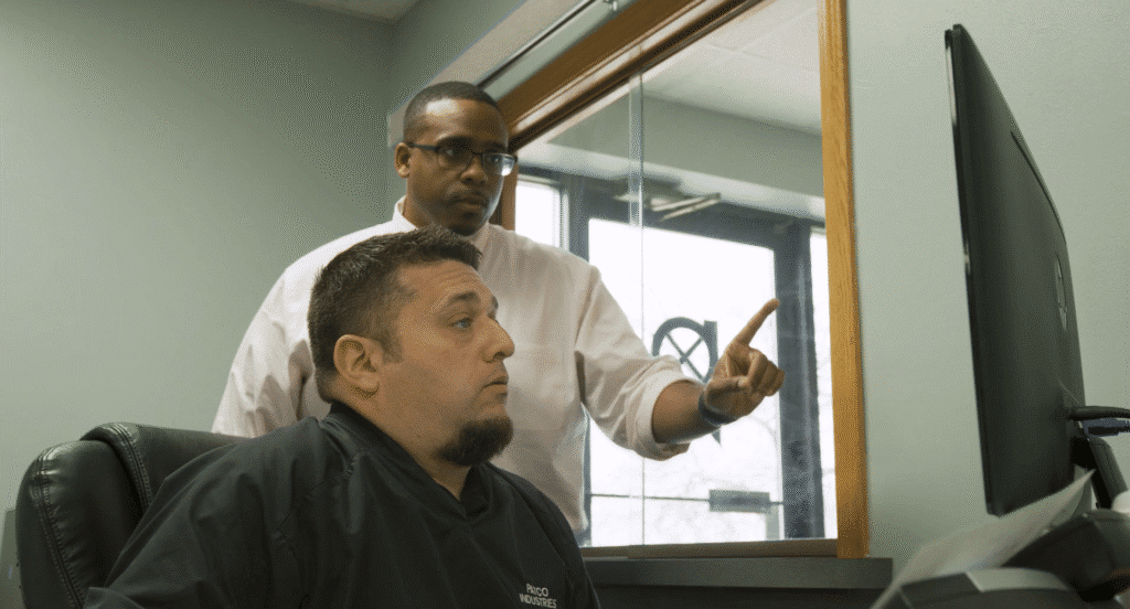 Two workers operate a large green Guifil industrial shearing machine to cut a long sheet of brown metal in a warehouse.