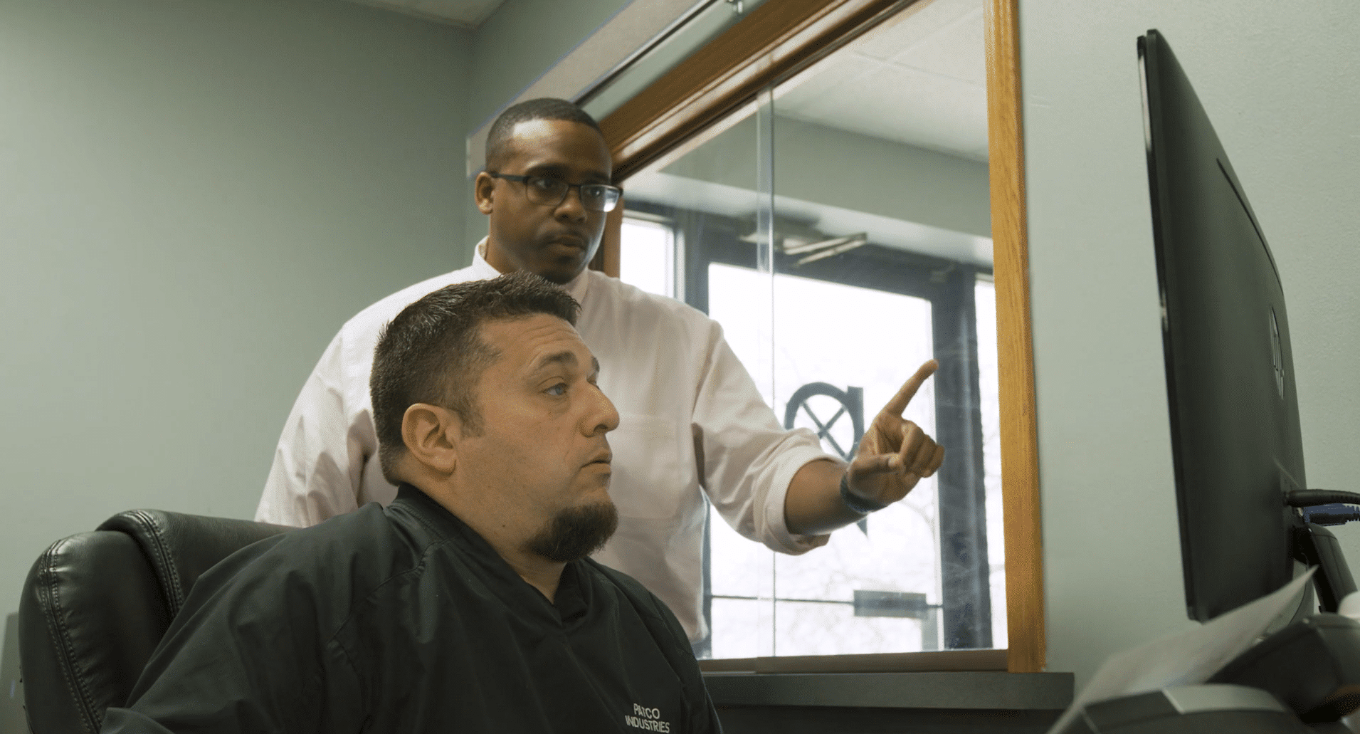 Two workers operate a large green Guifil industrial shearing machine to cut a long sheet of brown metal in a warehouse.