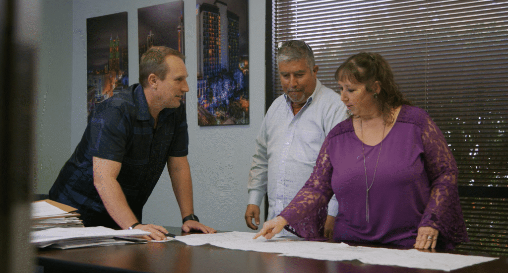 Three colleagues gather around a conference table to review architectural blueprints.
