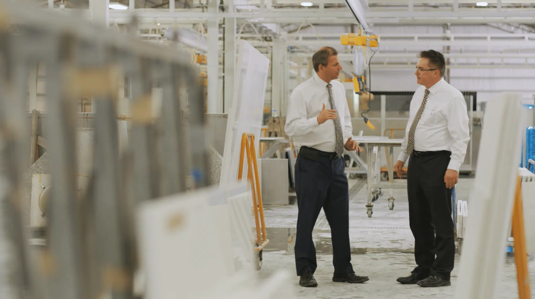Two men in white shirts and ties discuss operations while standing on a large factory floor to prevent burnout.