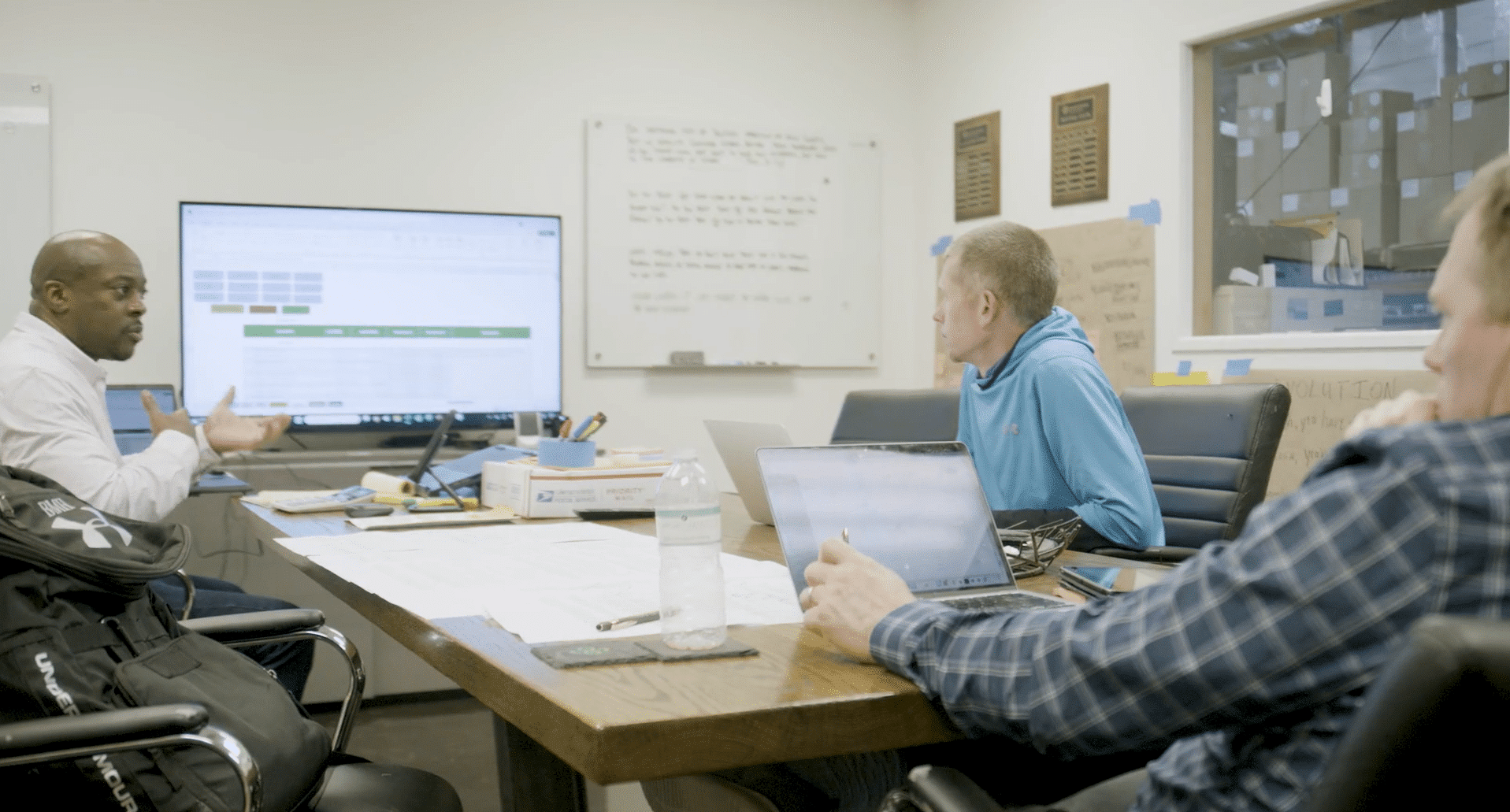 Three men around a conference table looking at cash flow and KPIs on screens.