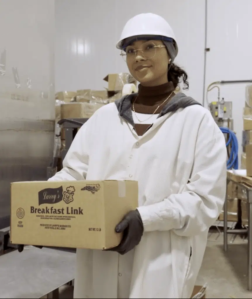 A smiling female factory worker holding a box of sausage ready to be shipped business consulting
