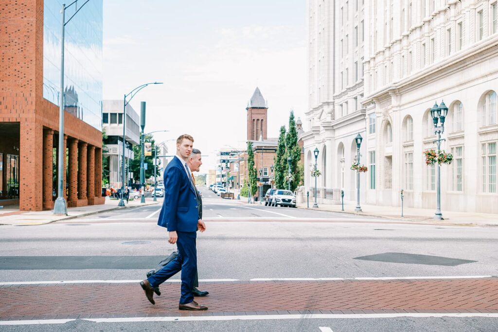 Two men wearing suits cross a downtown street in Greensboro NC