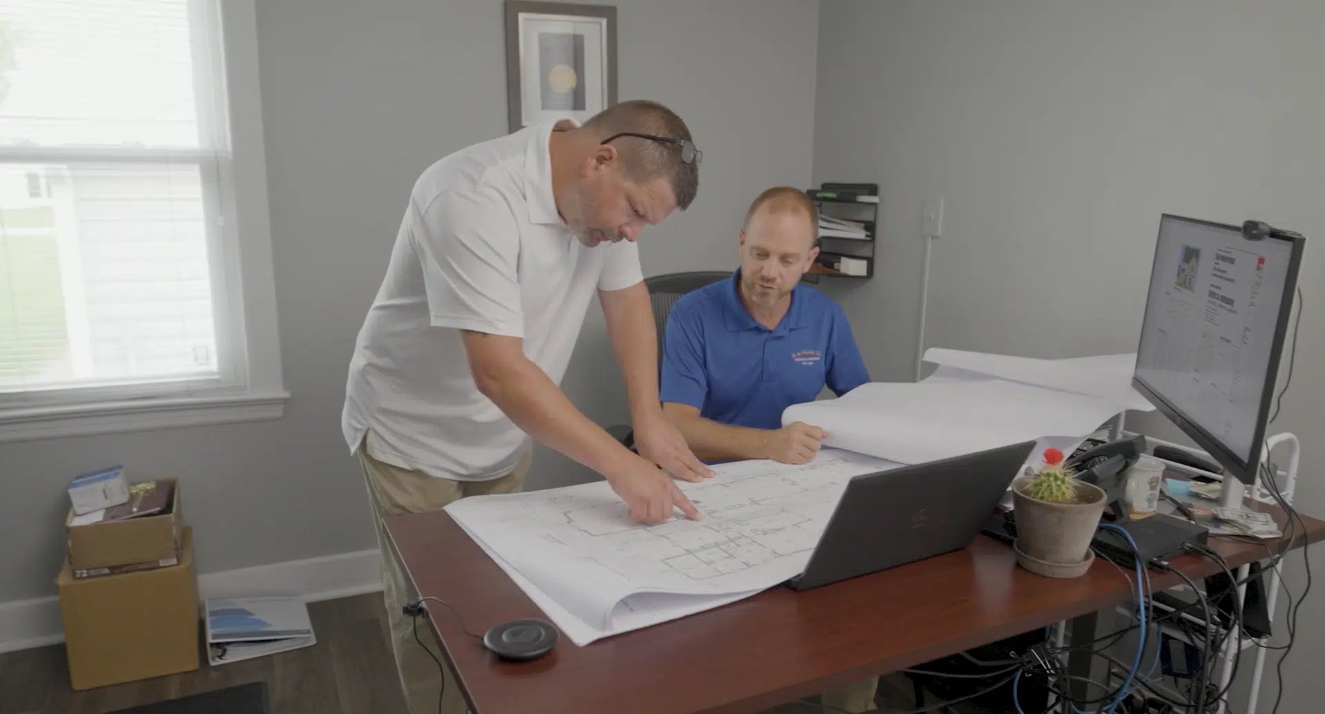 Two engineers examining blueprints at a desk in an office