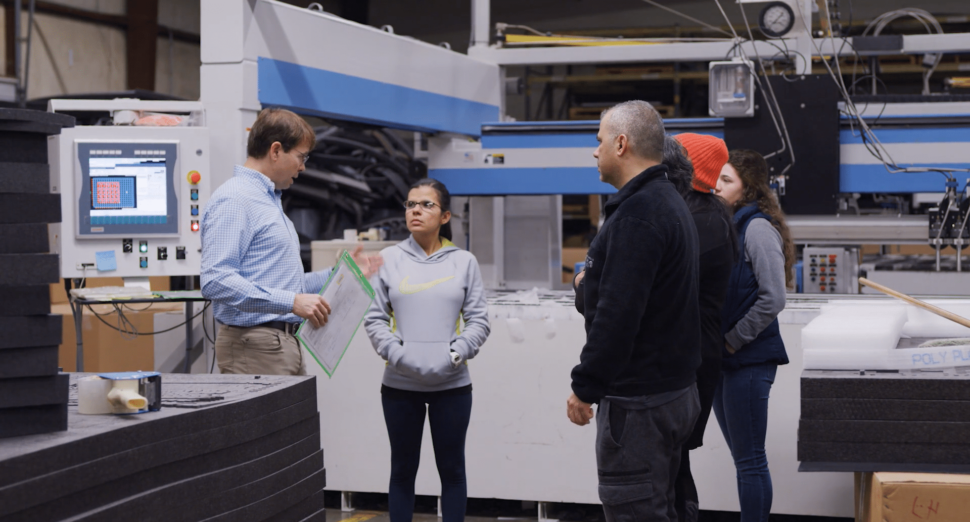 A group meeting on the floor of a manufacturing plant, led by a strategic operator.