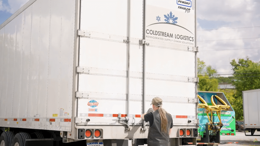 A driver closing the back gate of a semi-truck for transport.