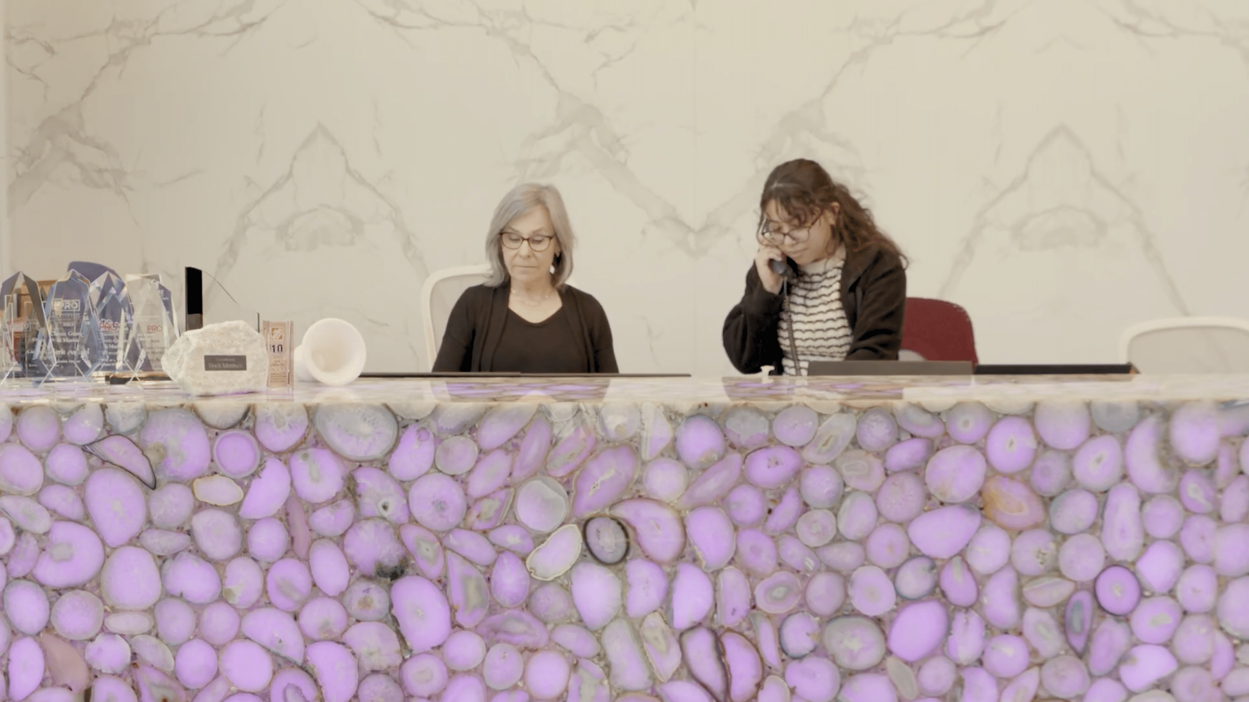 Two employees at a marble and granite company working behind an illuminated stone front desk
