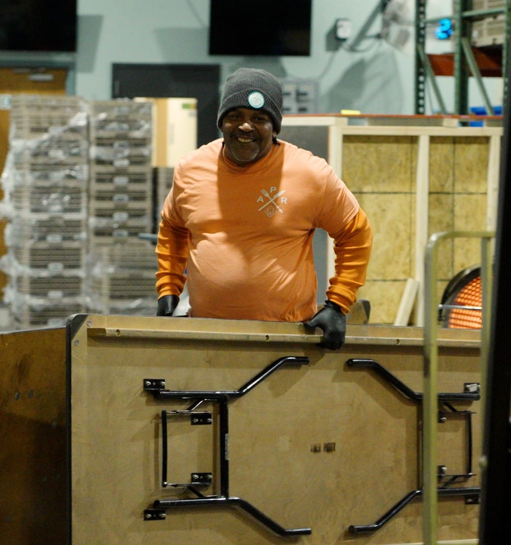 A warehouse employee smiling while carrying tables.