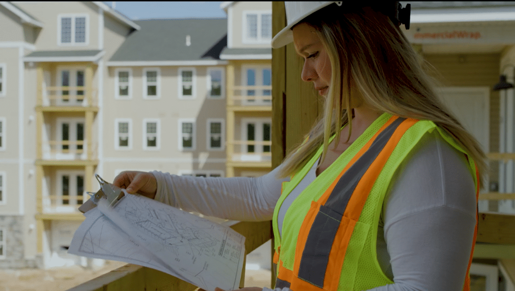A contractor in safety gear studying project plans while standing in a job site
