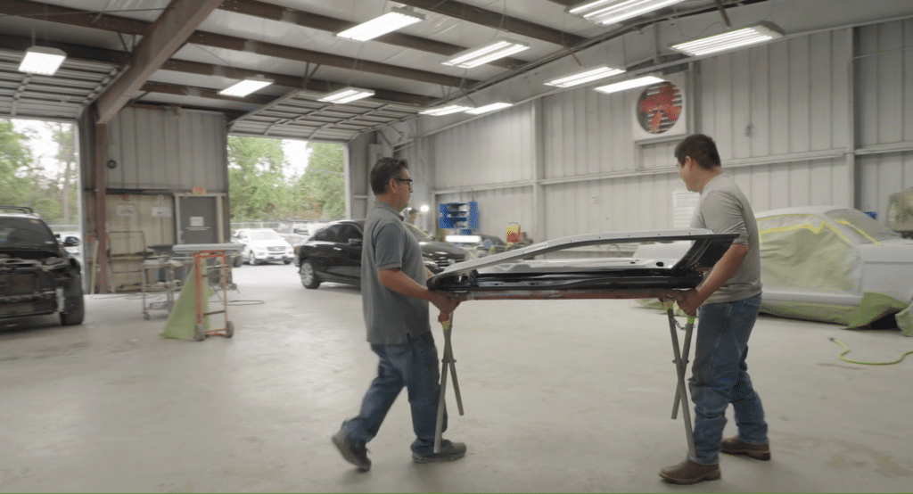 Two body shop employees carrying a car part