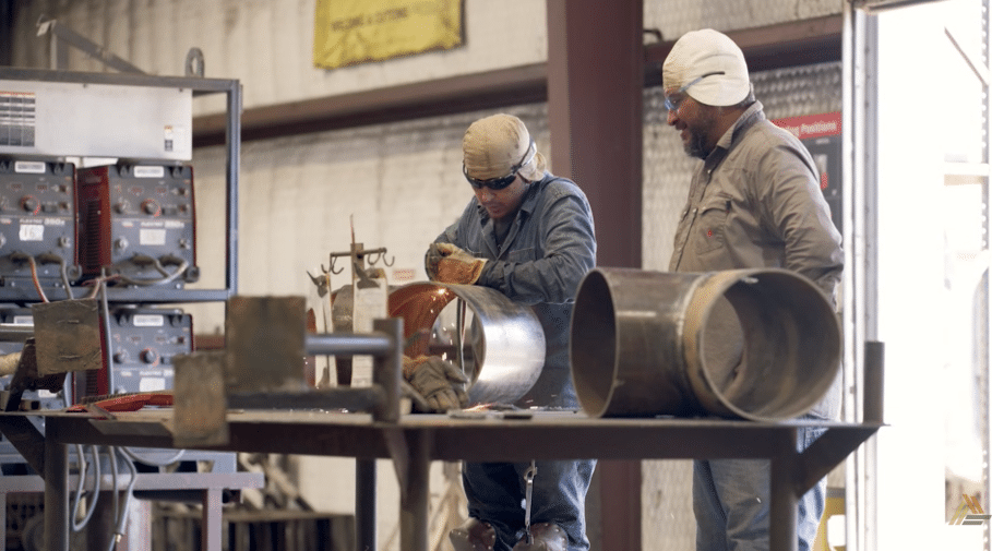Two welders in safety gear working on a large diameter metal pipe