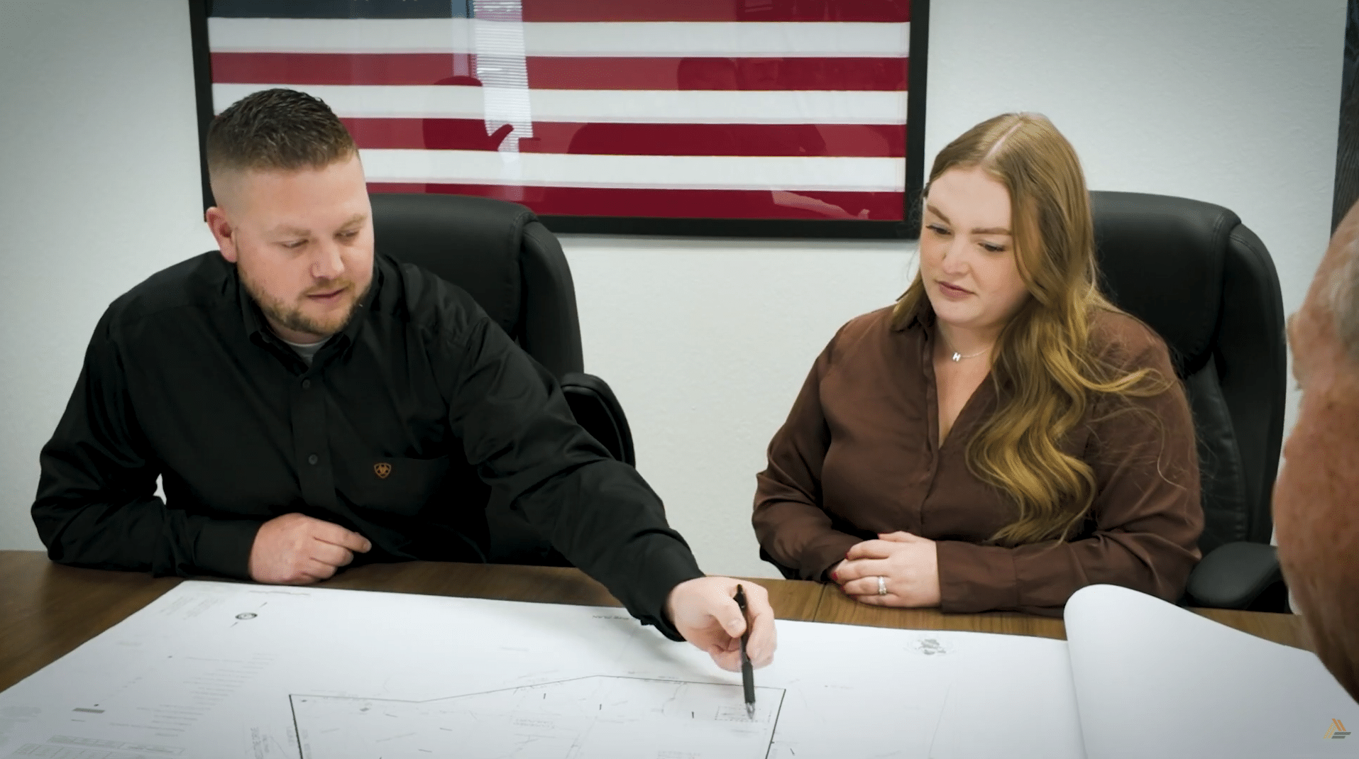 Two employees seated at a conference table going over blueprints.