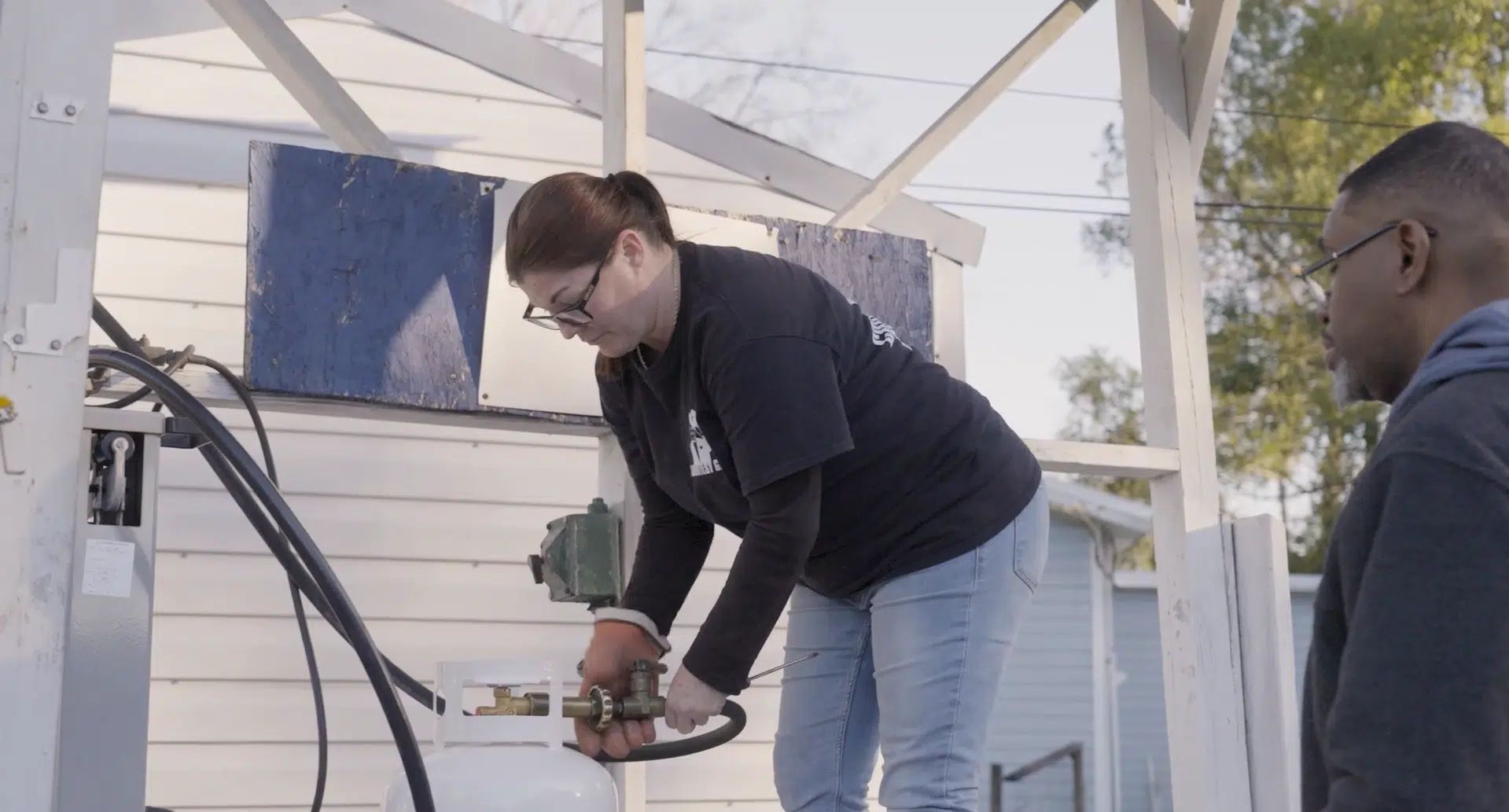 A utilities company employee is connecting a line to a gas tank.
