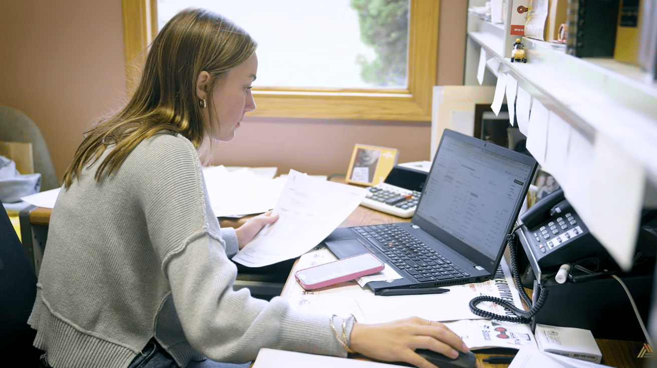 An office employee sitting at a messy desk reviewing her laptop screen.